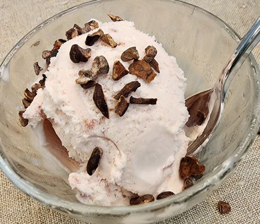cacao nibs sprinkled on strawberry ice cream in a glass bowl