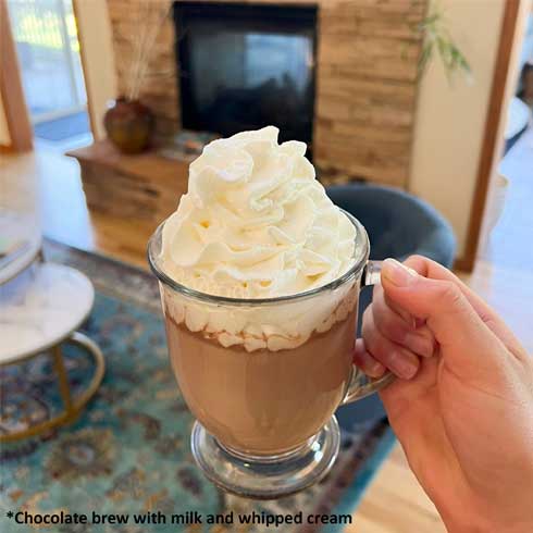 woman holding mug of brewed cacao with creamer and whipped cream in a rustic location with fireplace
