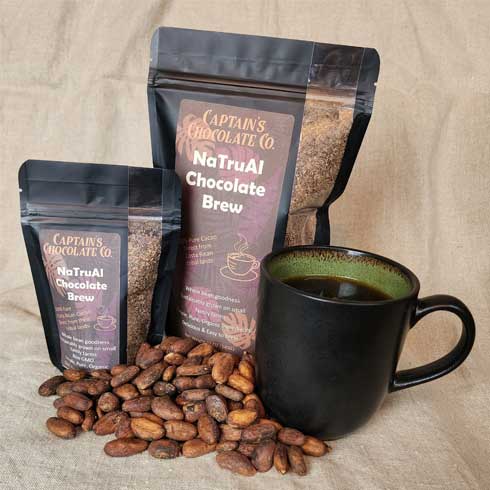 brewed cacao in a mug next to two bags of cacao brew and roasted cacao beans laid in front with burlap backgrop