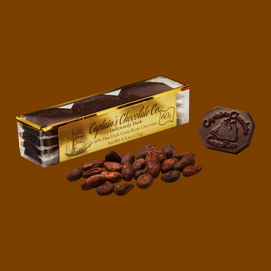 small rectangular translucent box set of chocolate medallions posing with roasted cacao beans and a loose medallion on a brown background