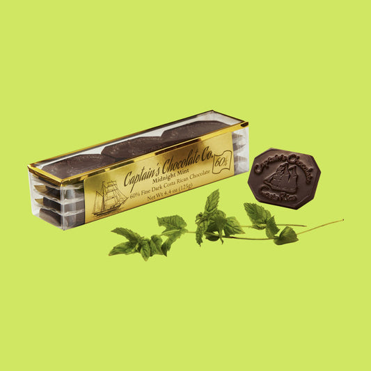small rectangular translucent box set of chocolate medallions posing with a mint leaf and a loose medallion on a green background