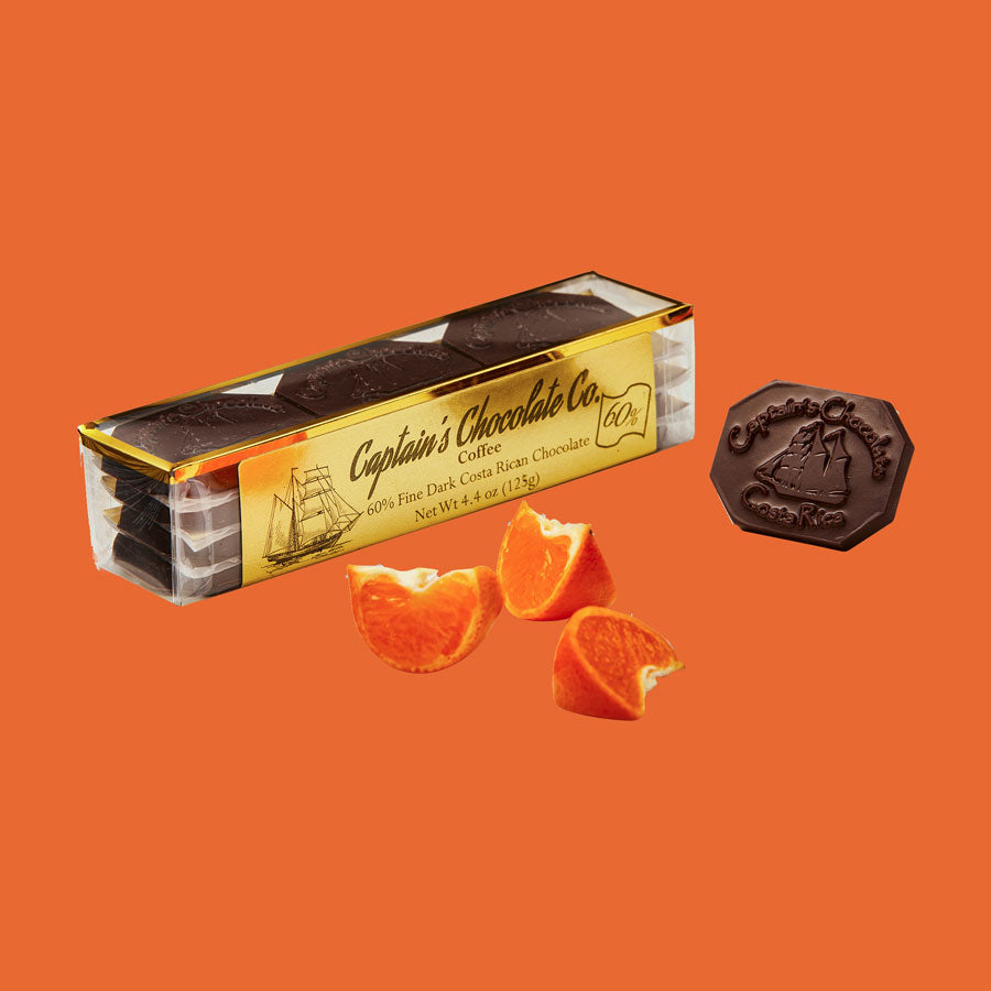 small rectangular translucent box set of chocolate medallions posing with orange slices and a single medallion on an orange background