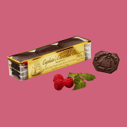 small rectangular translucent box set of chocolate medallions posing with raspberries and a single medallion on a fuchsia background